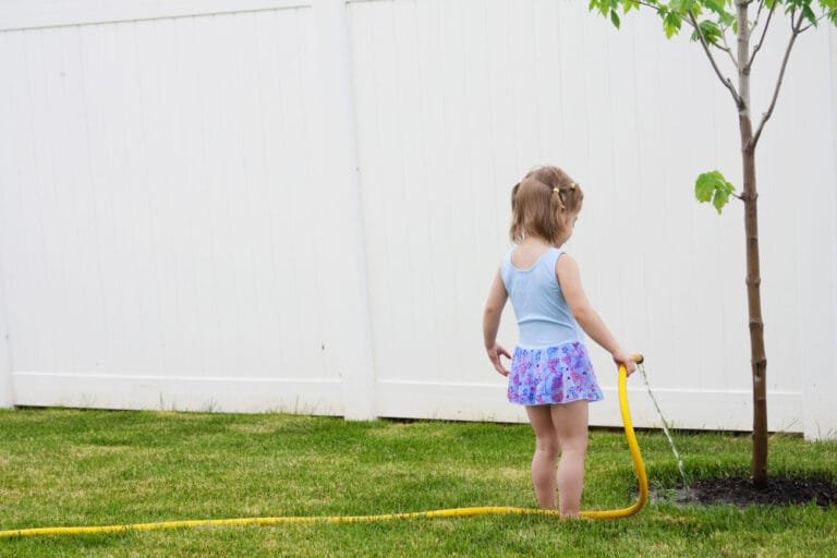 little girl waters a tree in her yard